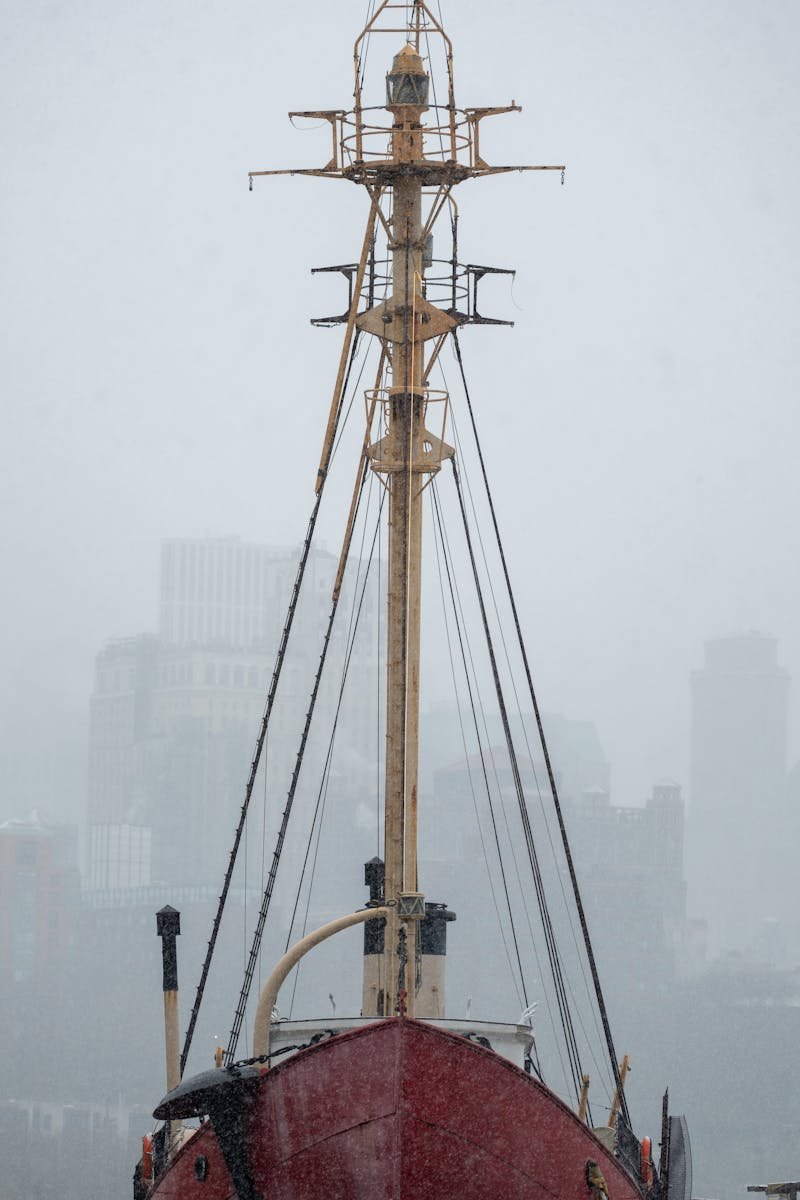 Red Ship Mast Amid Snowstorm with City Backdrop